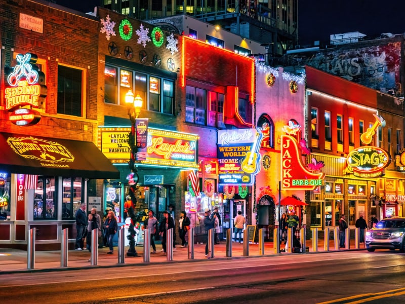 A group of people walking on a sidewalk in front of a building with neon signs