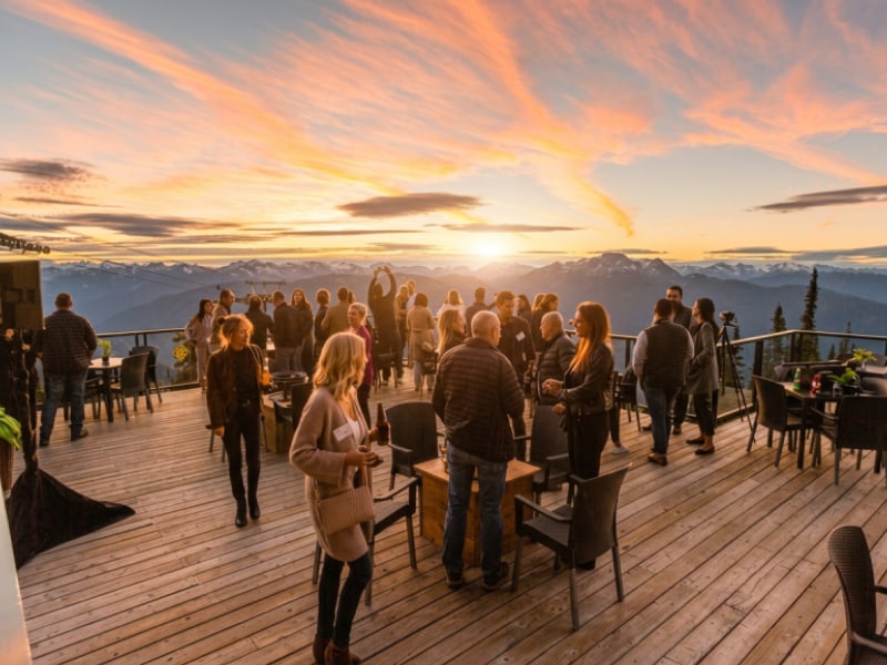 People mingling on mountain deck at sunset overlooking snowy peaks