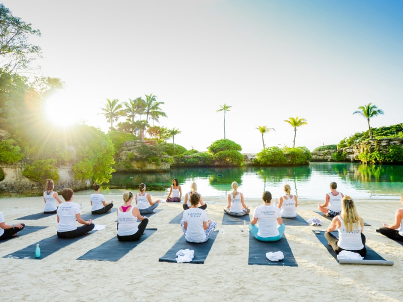 Group practicing yoga on mats along a tropical beach