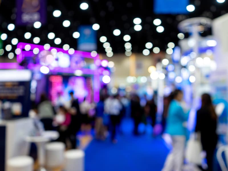 Blurred trade show floor with booths and attendees walking through aisle