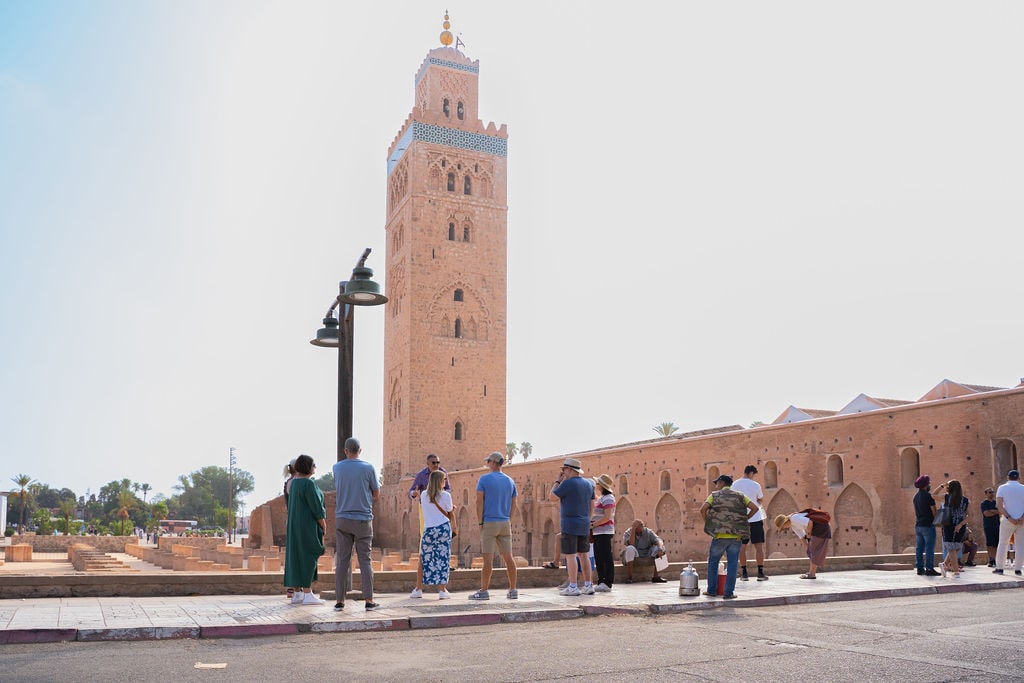 A group of people standing on a sidewalk near a tall tower
