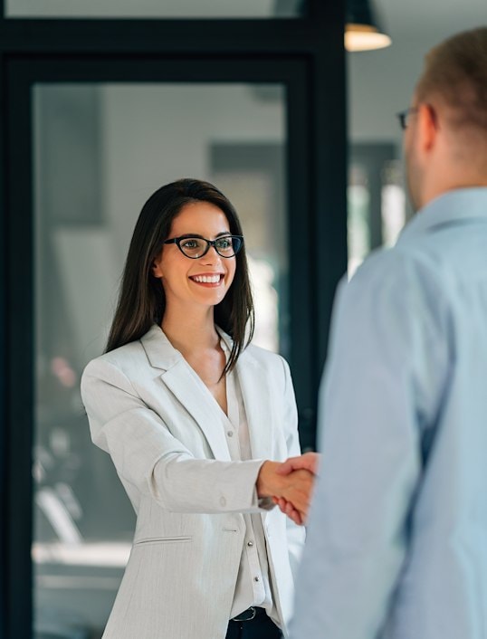 A woman in glasses shaking hands with a man in a suit