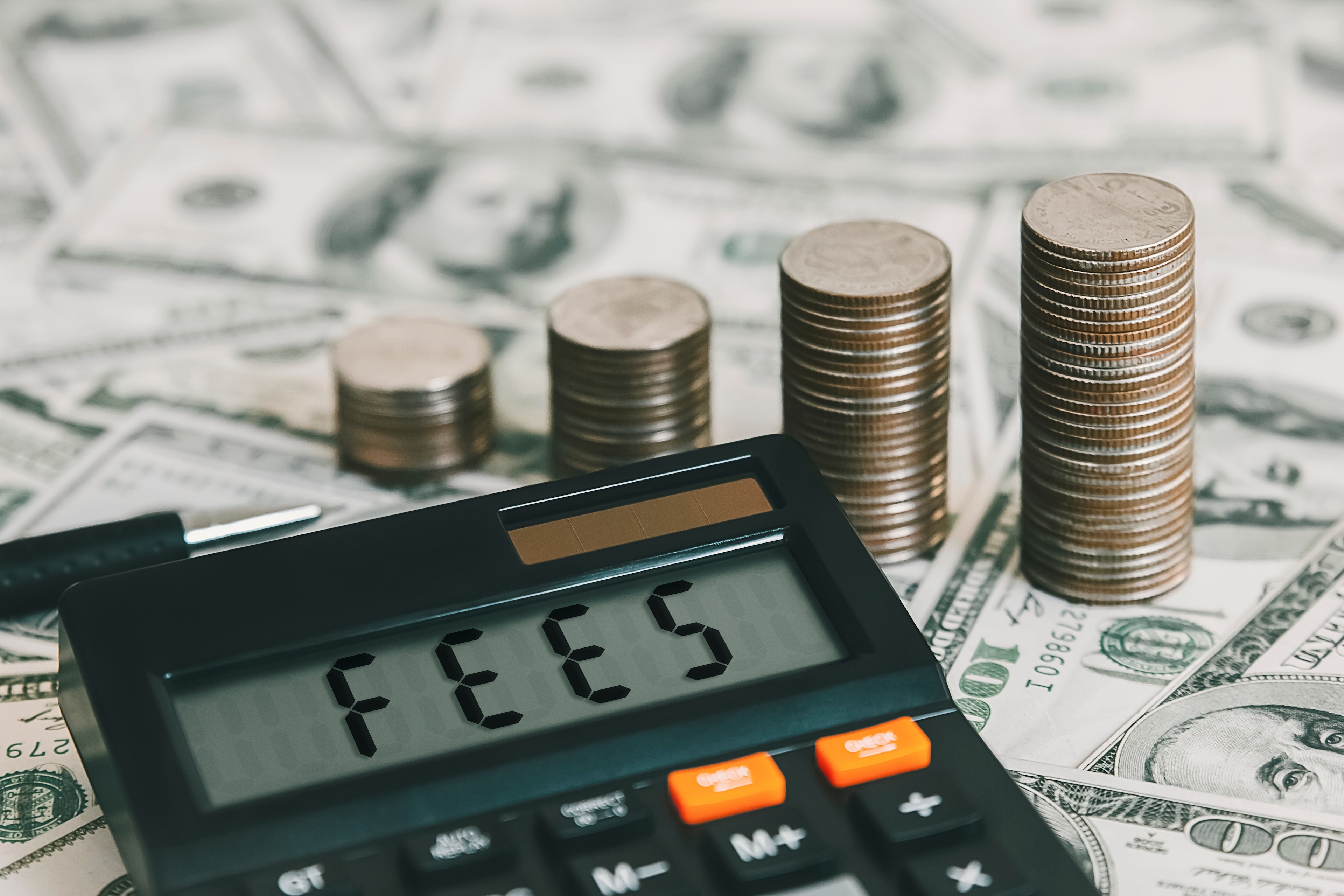 Calculator with stacks of dollars and change with the word fees on the calculator