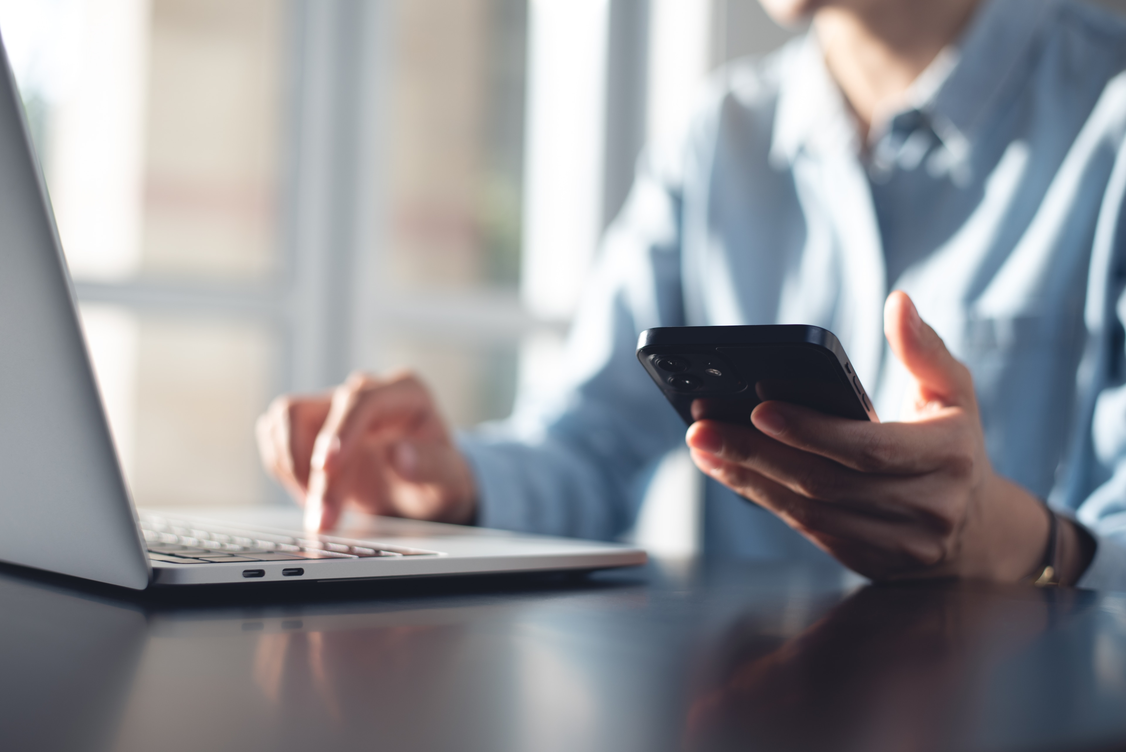 Business owner on her phone and laptop reviewing online banking dashboard