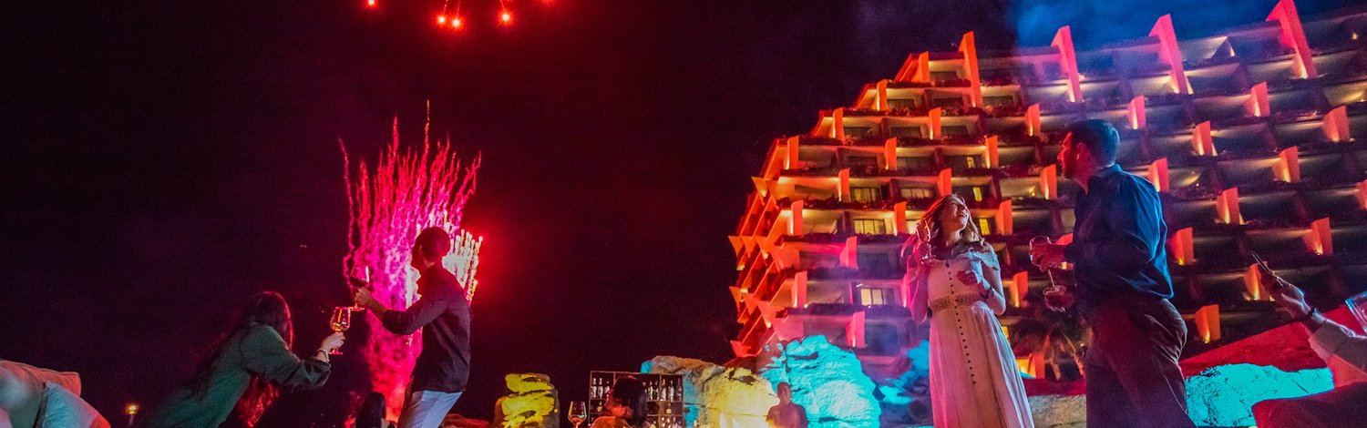 Personas reunidas alrededor de una fogata nocturna con fuegos artificiales, Grand Velas Los Cabos, Cabo San Lucas, México.