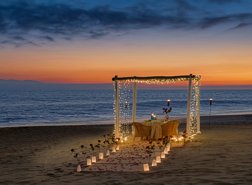 A table set up on a beach with candles and flowers