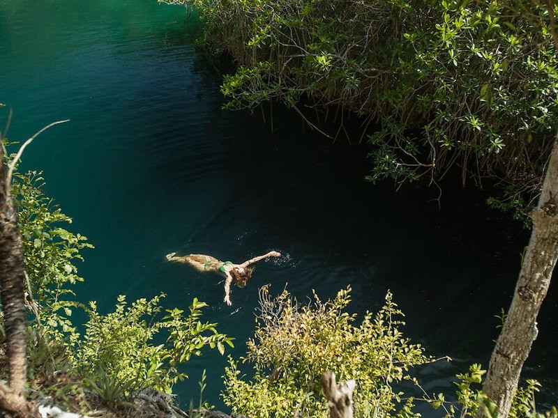 Woman in a straw hat relaxing in an infinity pool overlooking a lush jungle.