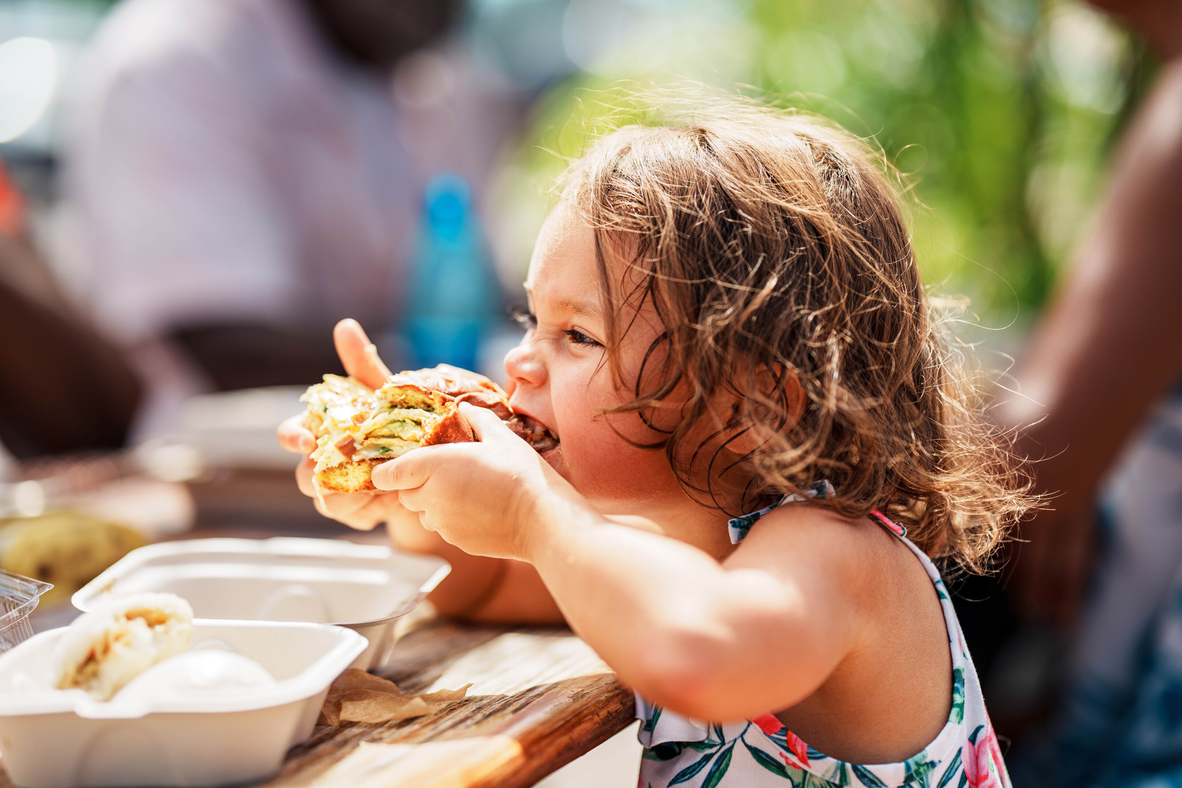 A little girl eating a sandwich at a picnic table