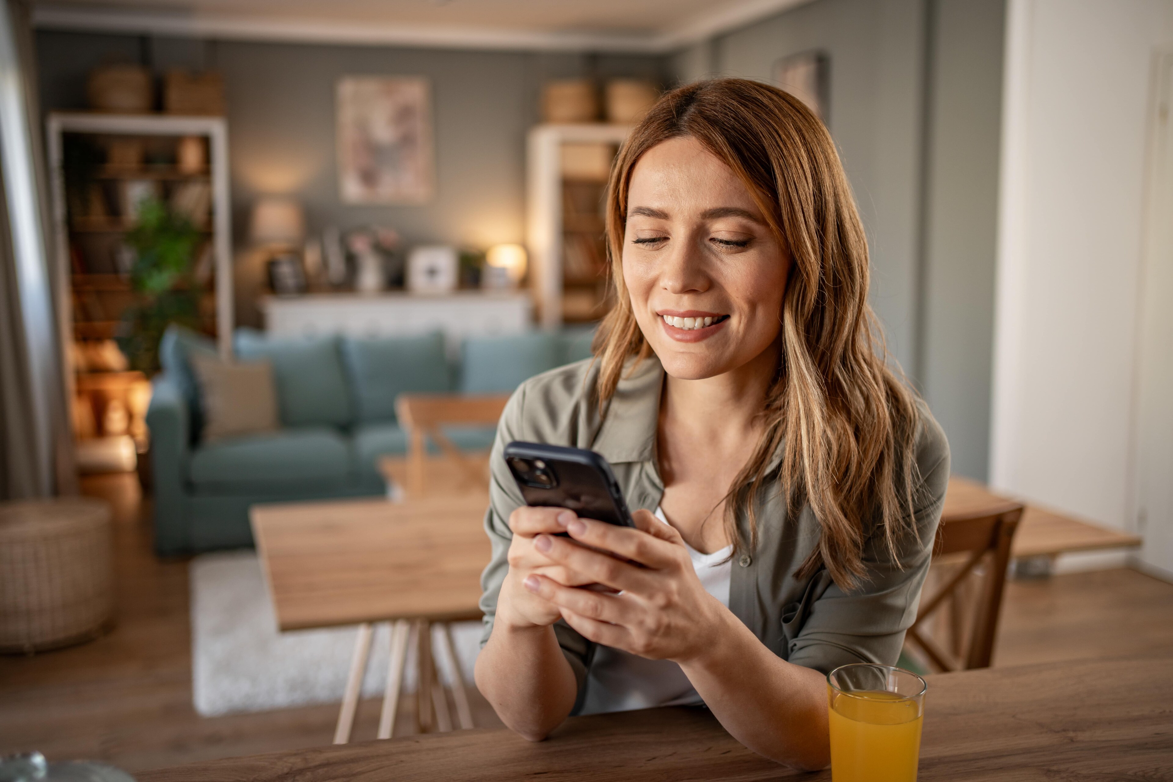 A woman smiles while using her phone in her home