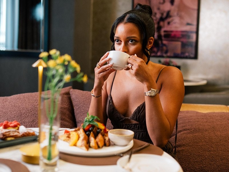 A woman sitting at a table drinking from a cup