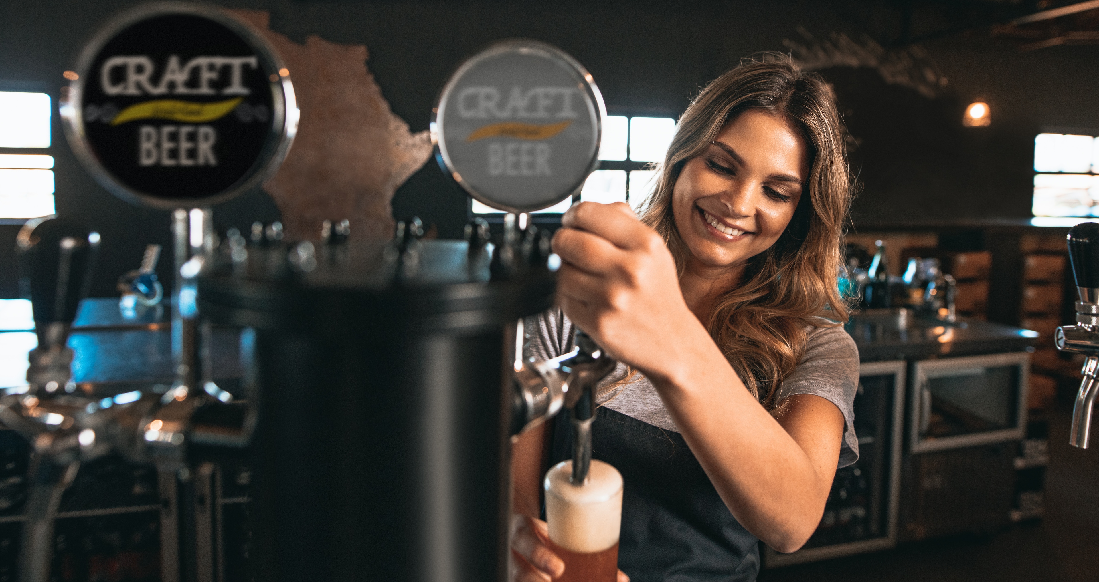 A woman pouring a glass of beer from a tap.