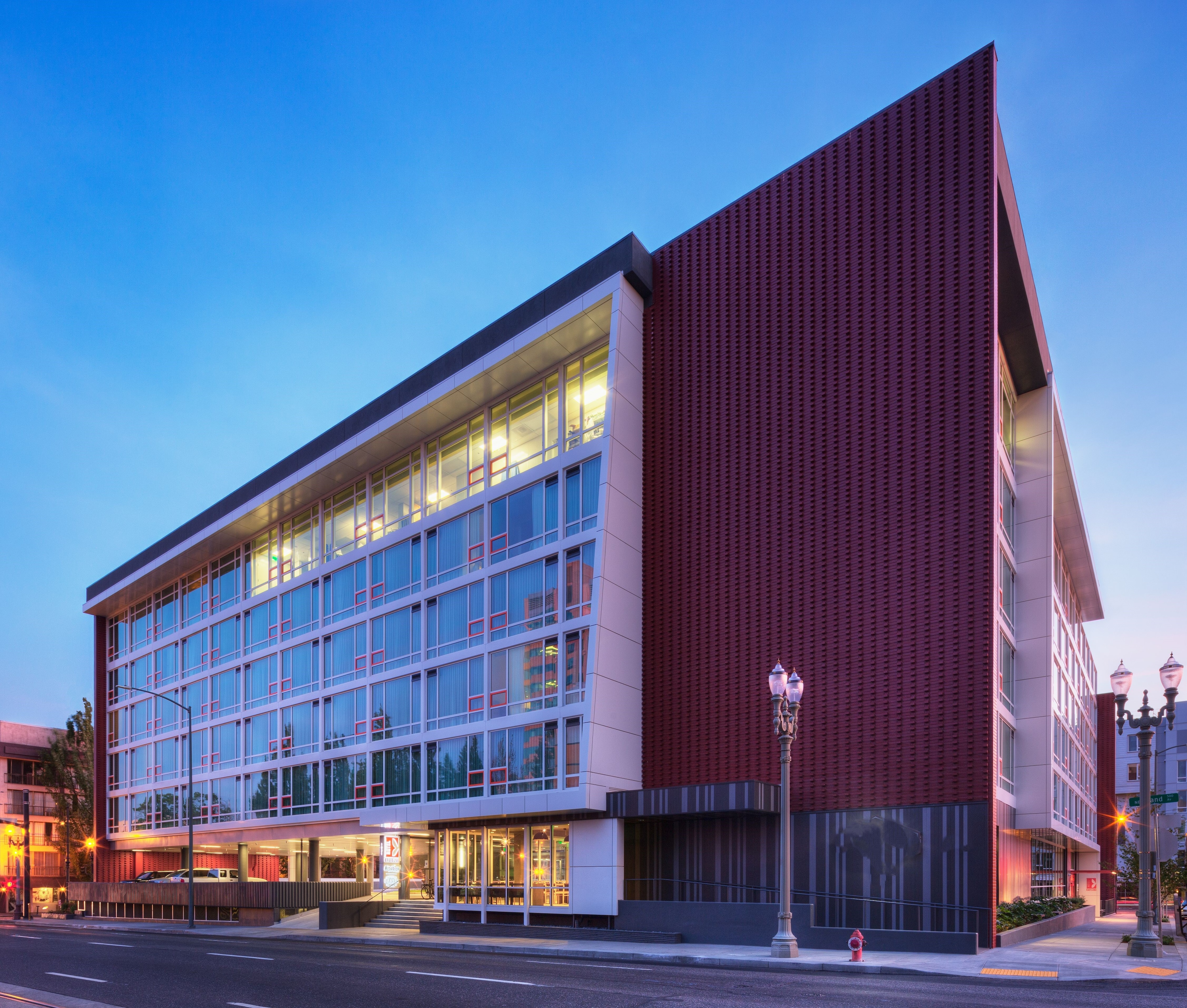 A large building with a red brick facade and glass windows, lit up at dusk.