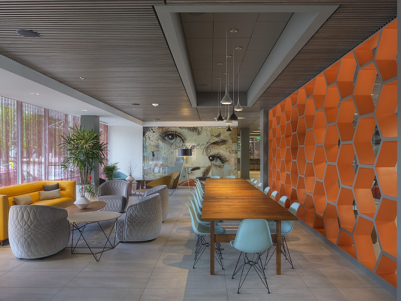 A modern meeting room with a large wooden table, blue chairs, and an orange accent wall.
