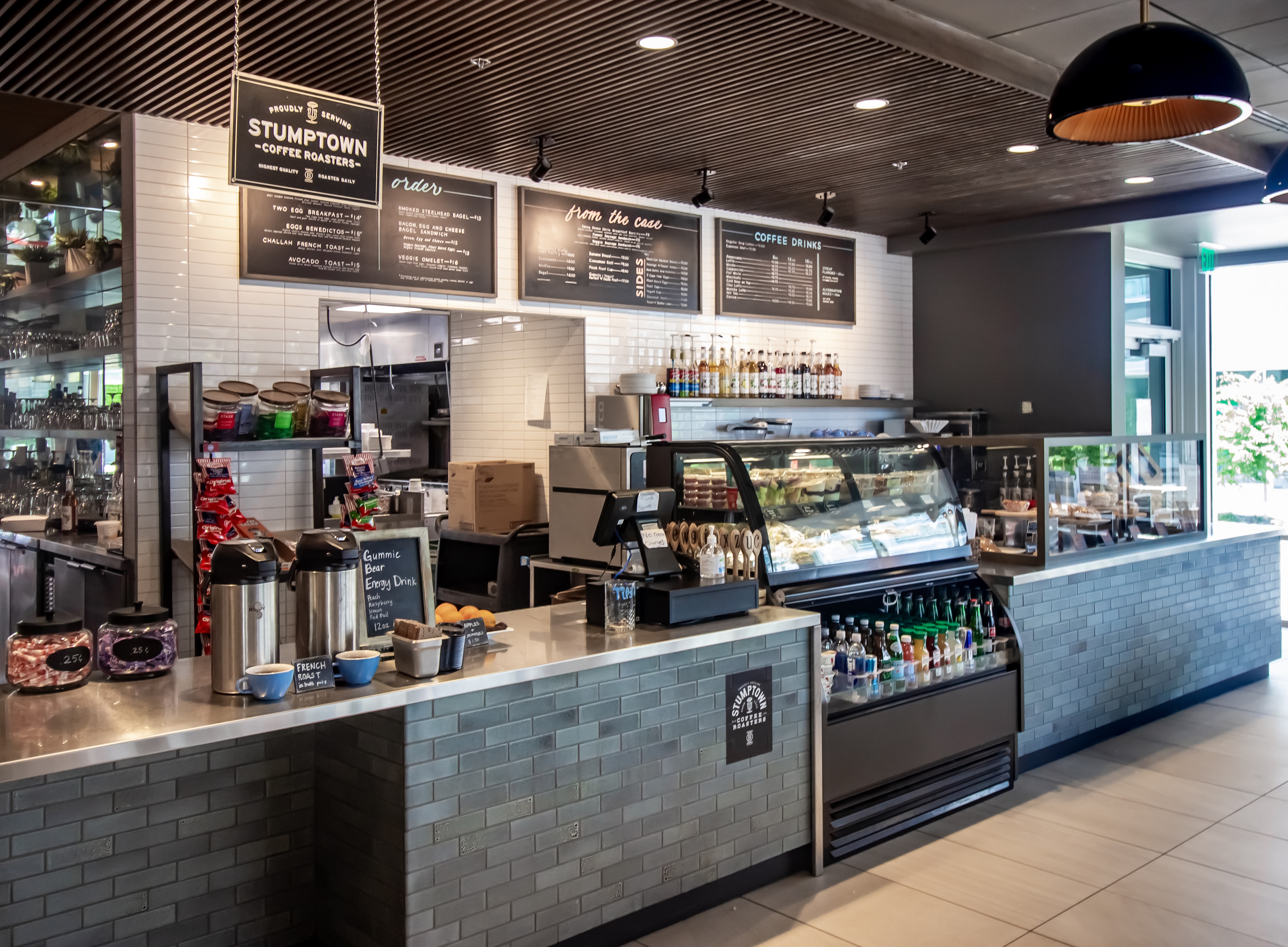 A coffee shop counter with a menu board, refrigerator, and various beverages and pastries.
