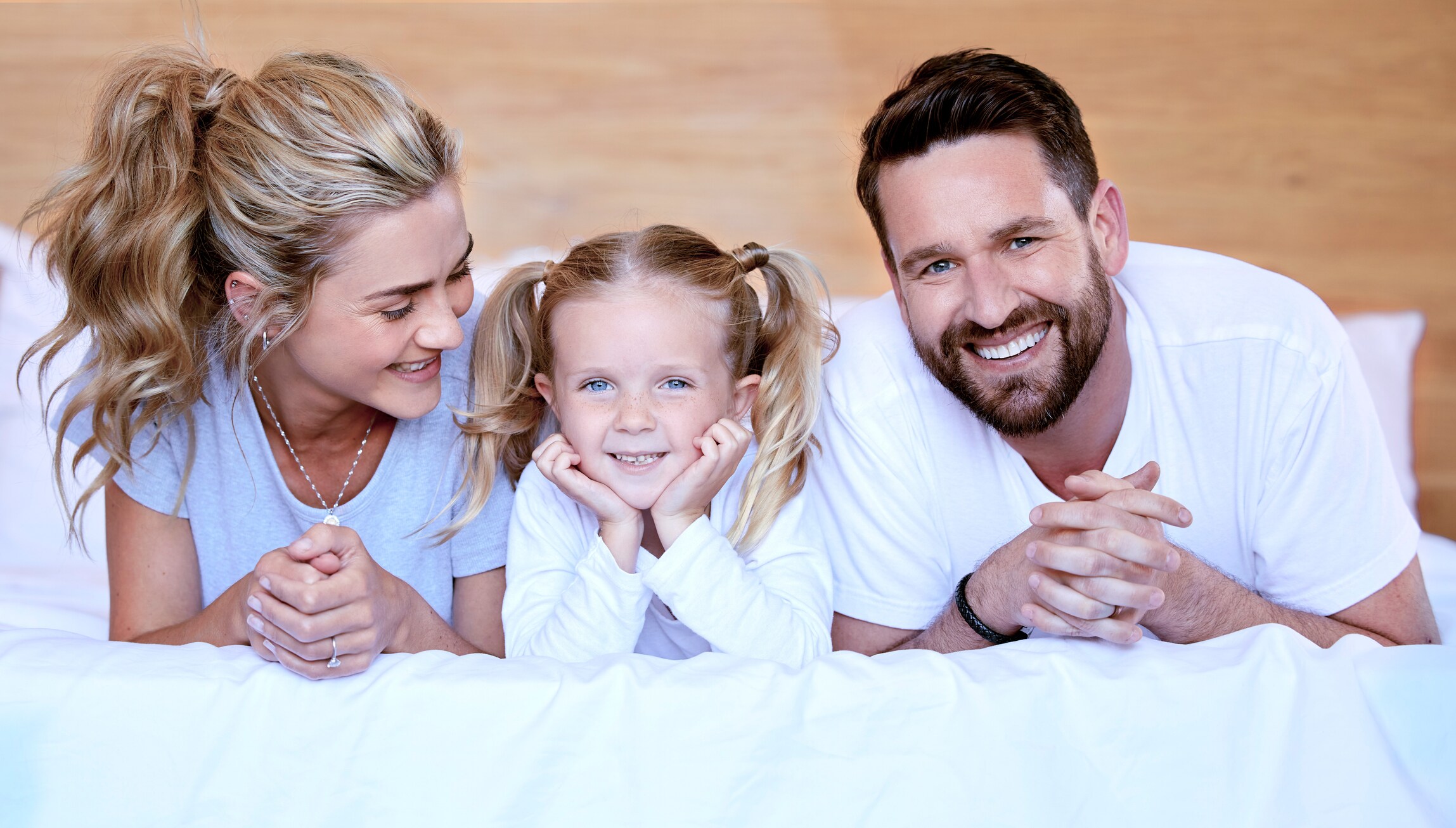 A young, smiling family of three, lying together on a hotel bed Hotel J, Green Bay, Wisconsin.