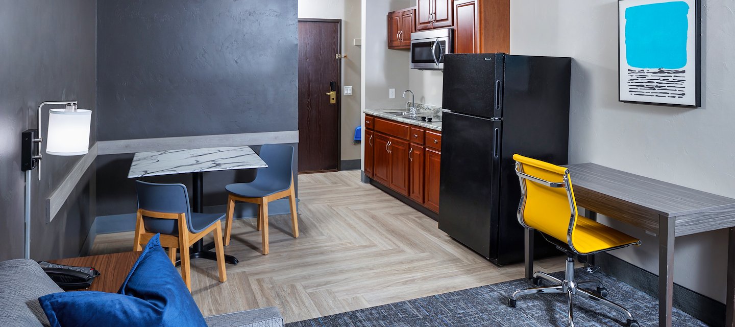 A hotel suite with a kitchenette, dining area, and a living space with a gray couch At Hotel J, Green Bay, Wisconsin