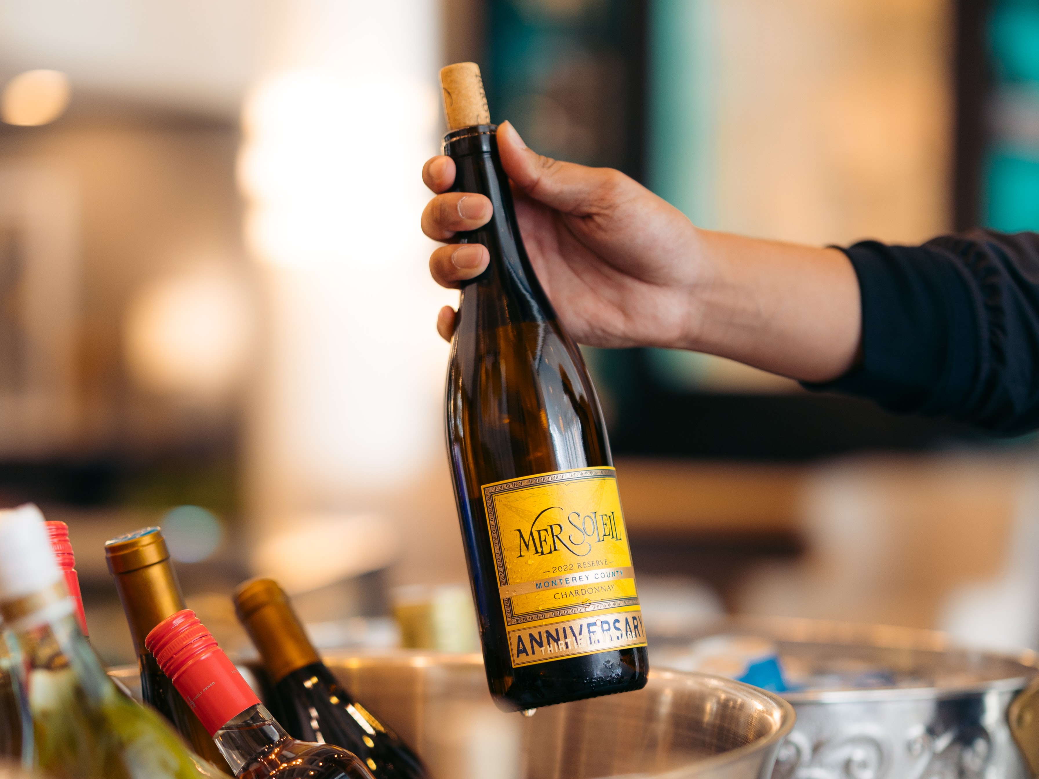 A hand holding a bottle of white wine over a counter with other wine bottles.