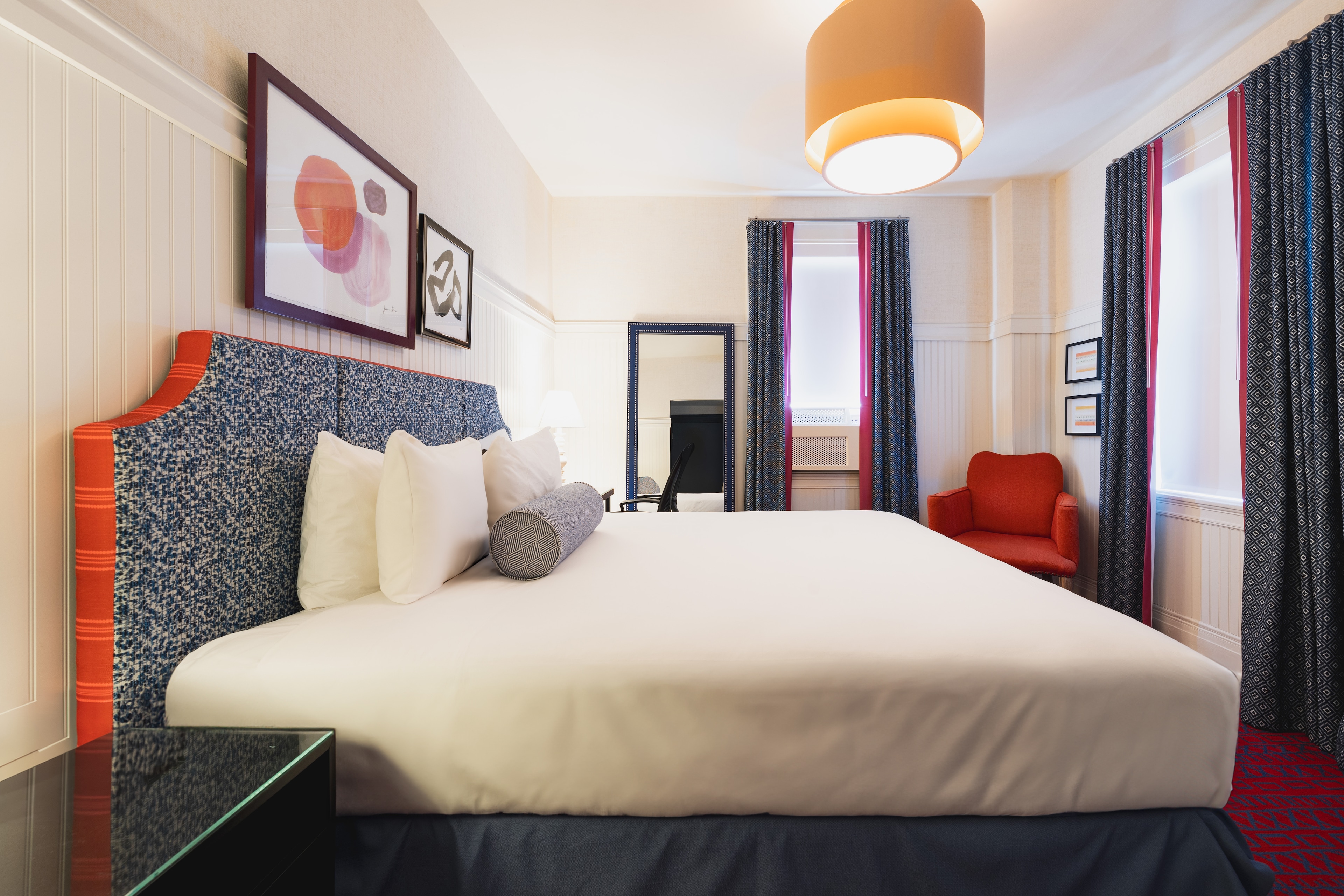 A hotel room with a large bed, red chair, and modern decor.