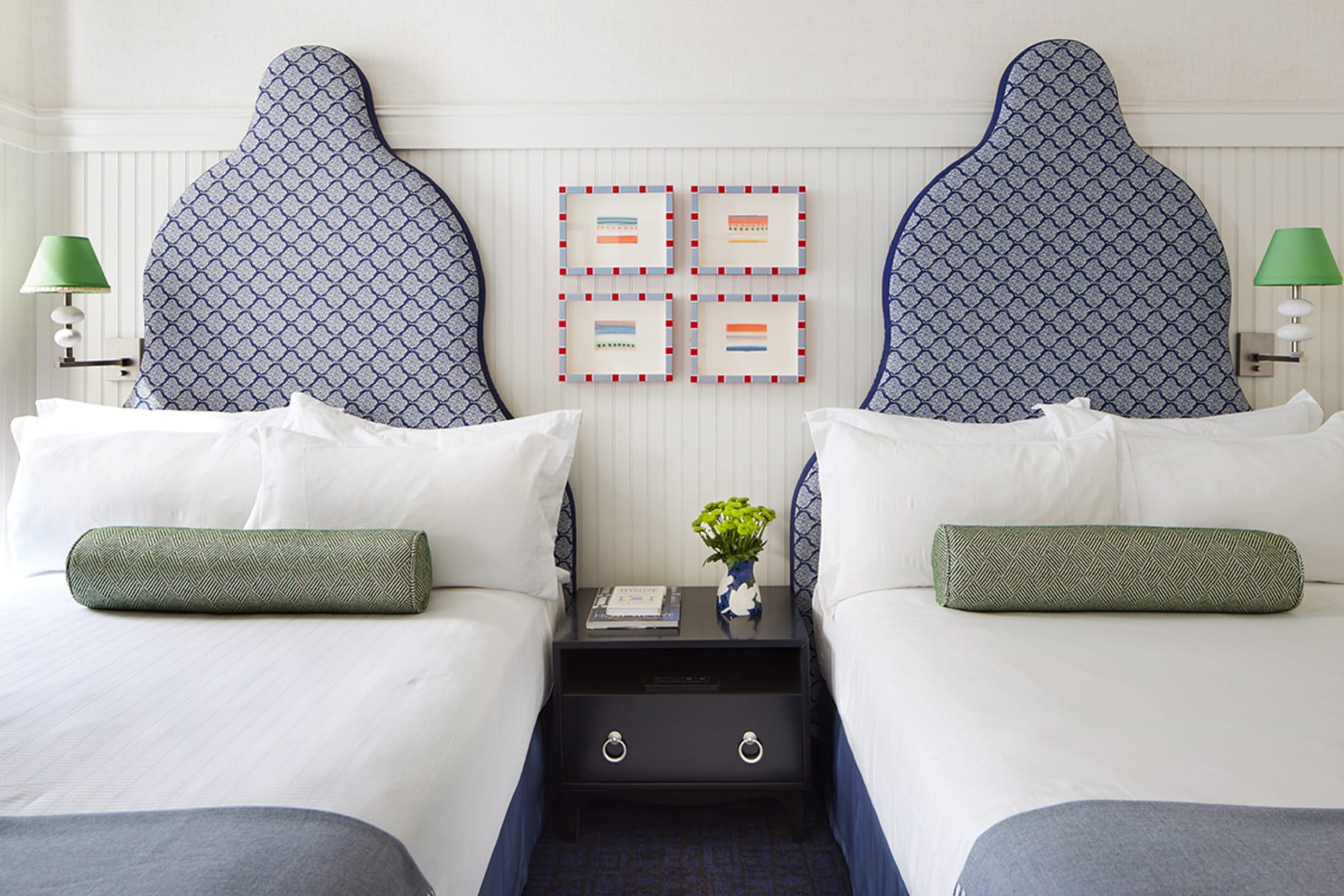 A hotel room with two beds, nightstand, and artwork