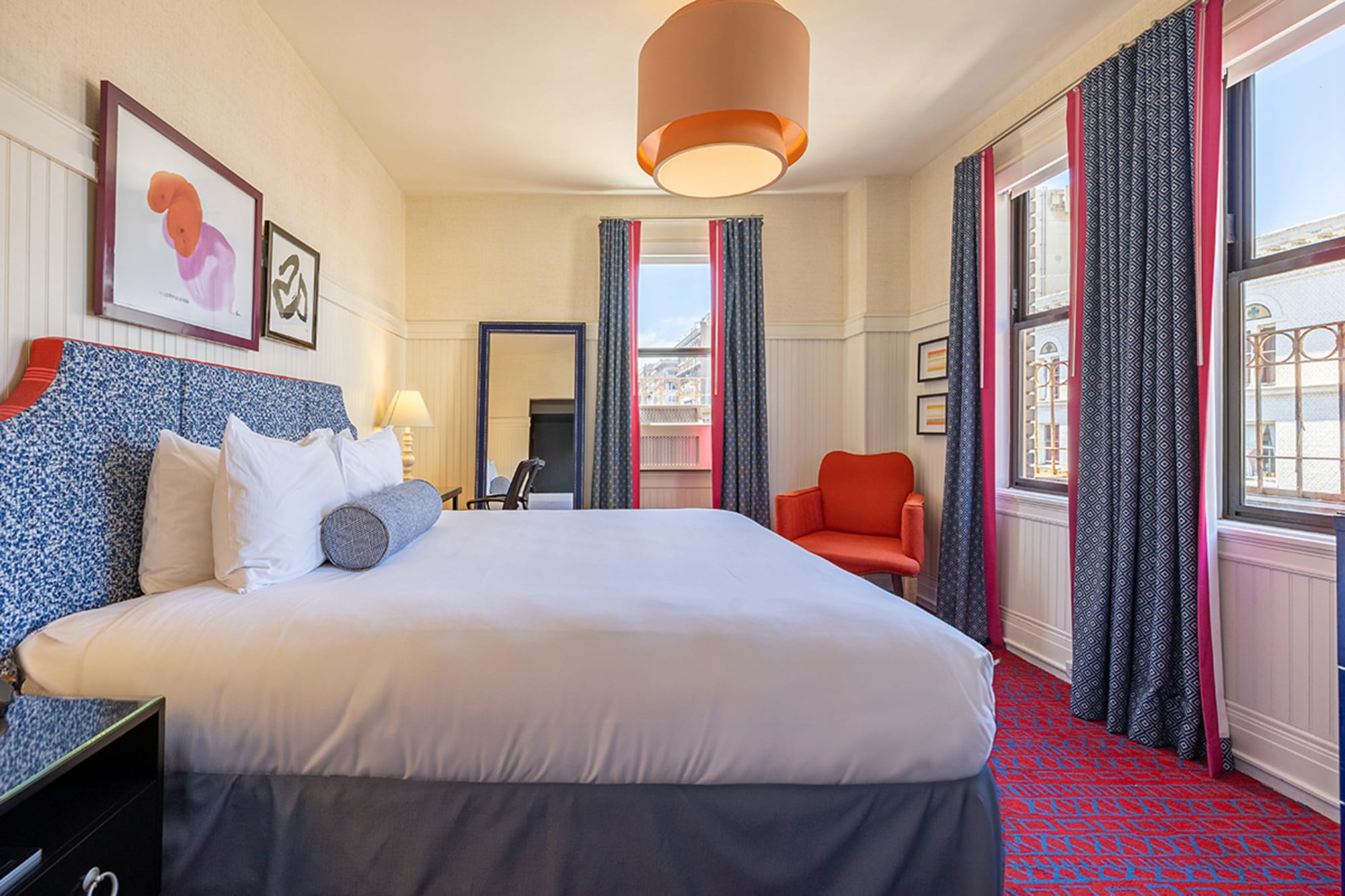 A hotel room with a large bed, window, chair, lamp, and artwork on the wall.