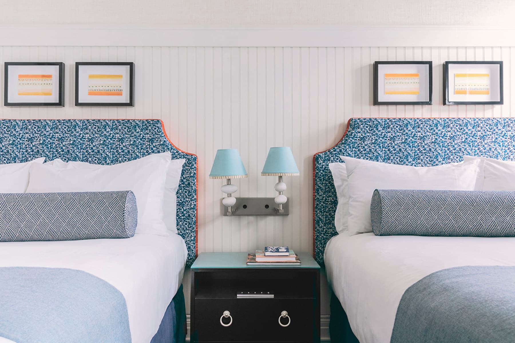 A hotel room with two beds, a nightstand, and artwork on the wall.