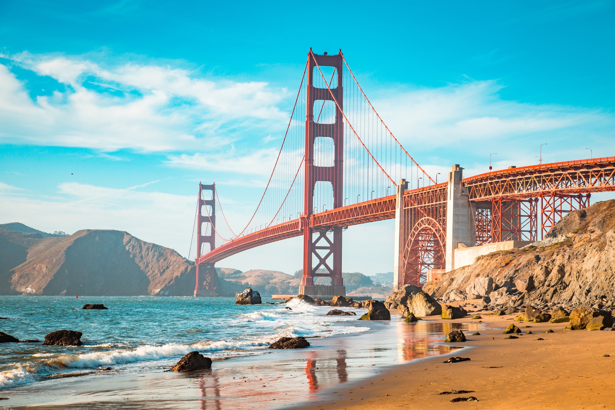 The Golden Gate Bridge over the ocean with waves crashing on the beach