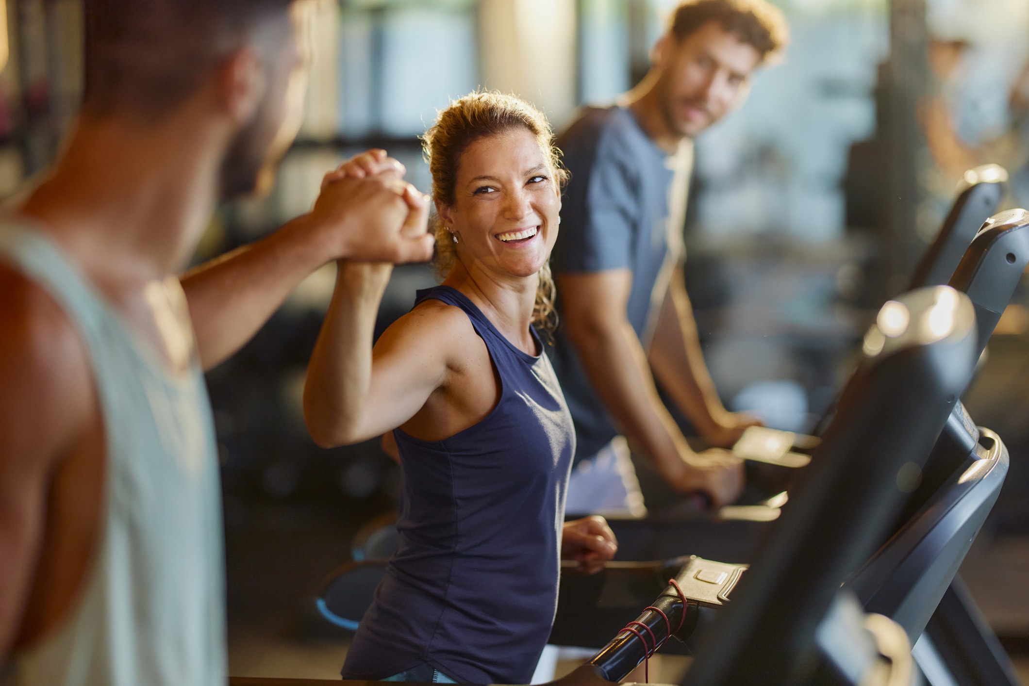 A woman and two men are exercising on treadmills in a gym.