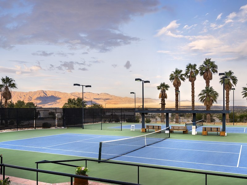 A tennis court with palm trees and mountains in the background