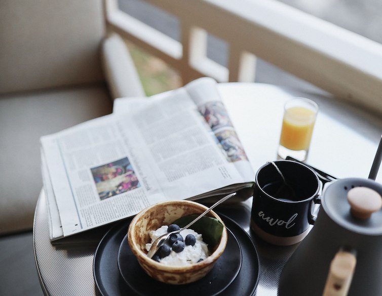 Breakfast with yogurt, blueberries, coffee, orange juice, and a newspaper on an outdoor table at AWOL Kennebunkport