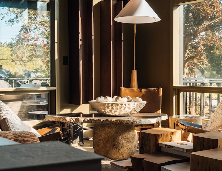 Sunlit AWOL hotel lounge with leather chairs, natural wood furnishings, and large windows overlooking the trees.