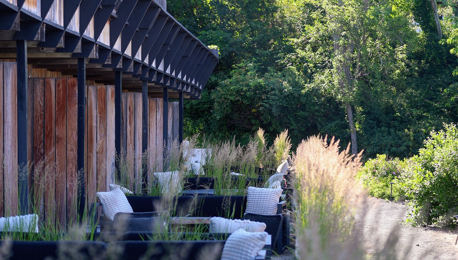 Outdoor seating areas surrounded by ornamental grasses and trees beside AWOL hotel 