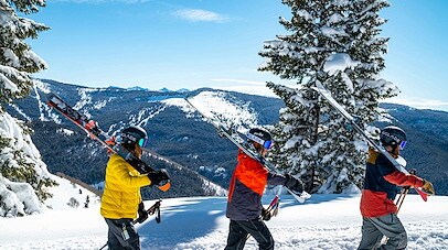 Three skiers walking in a line on a snow covered mountain with more mountains in the background 