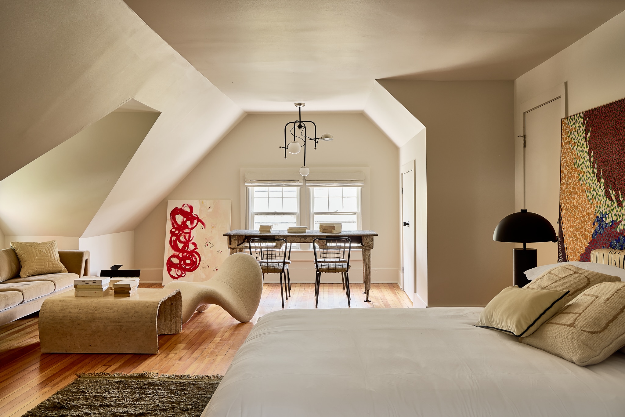 A wide view of a suite with a sofa, coffee table, dining table, chairs, bed, and artwork.