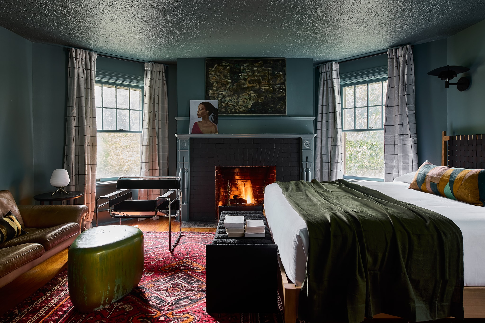 A cozy hotel room with a fireplace, bed, sofa, and chair.
