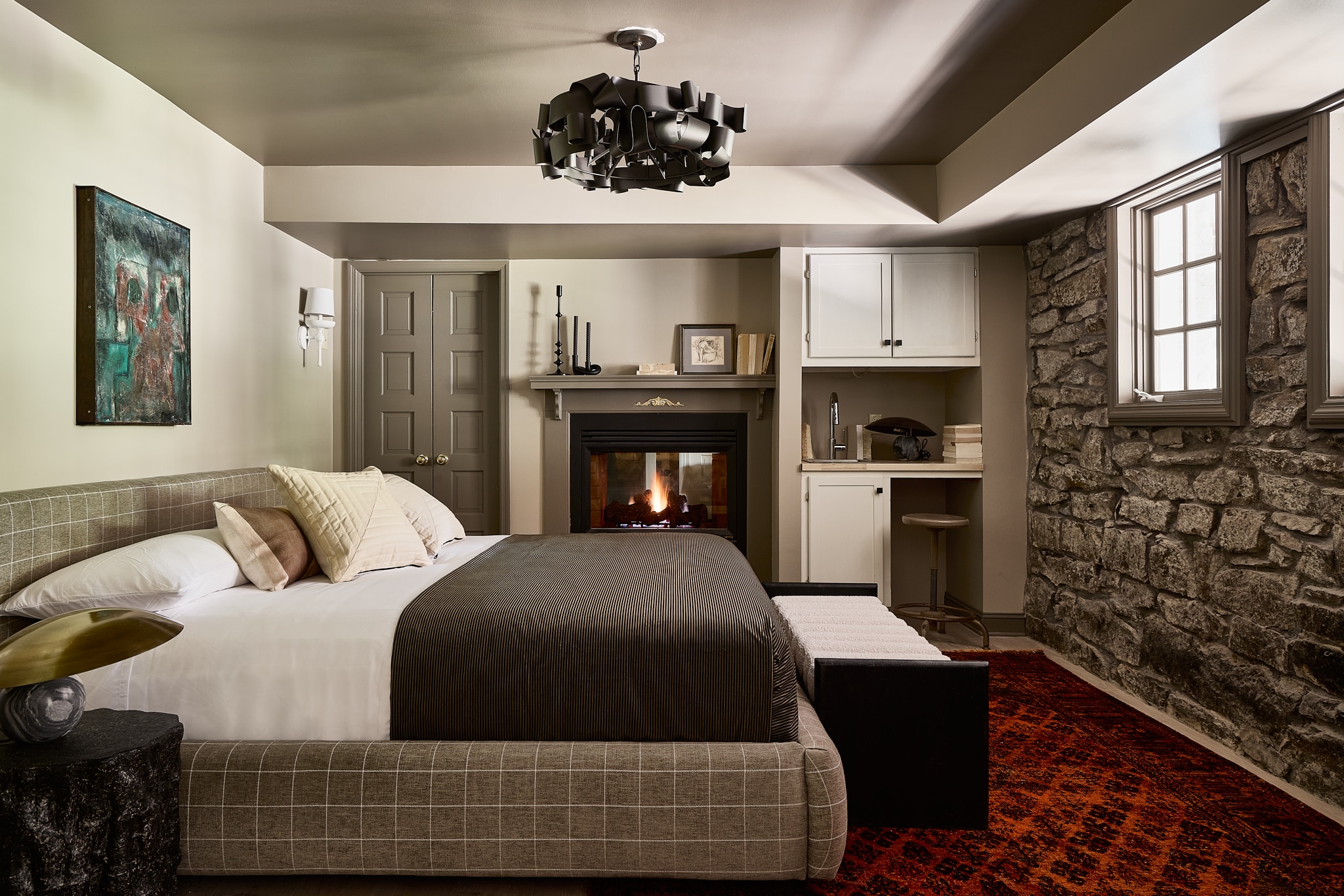 A hotel room with a bed, fireplace, stone wall, and window