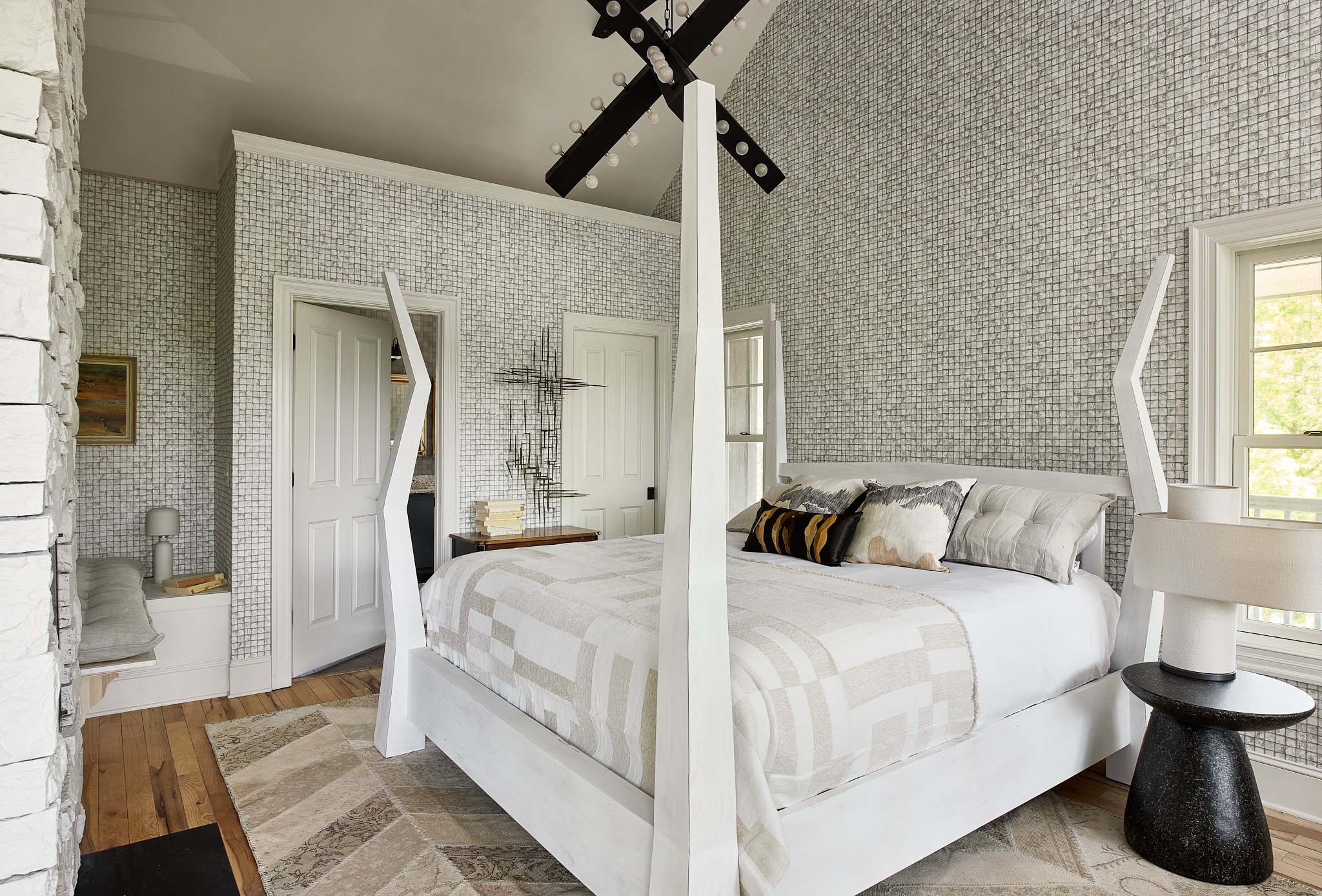 A wide view of a bedroom with a white four-poster bed, a window, and a door.