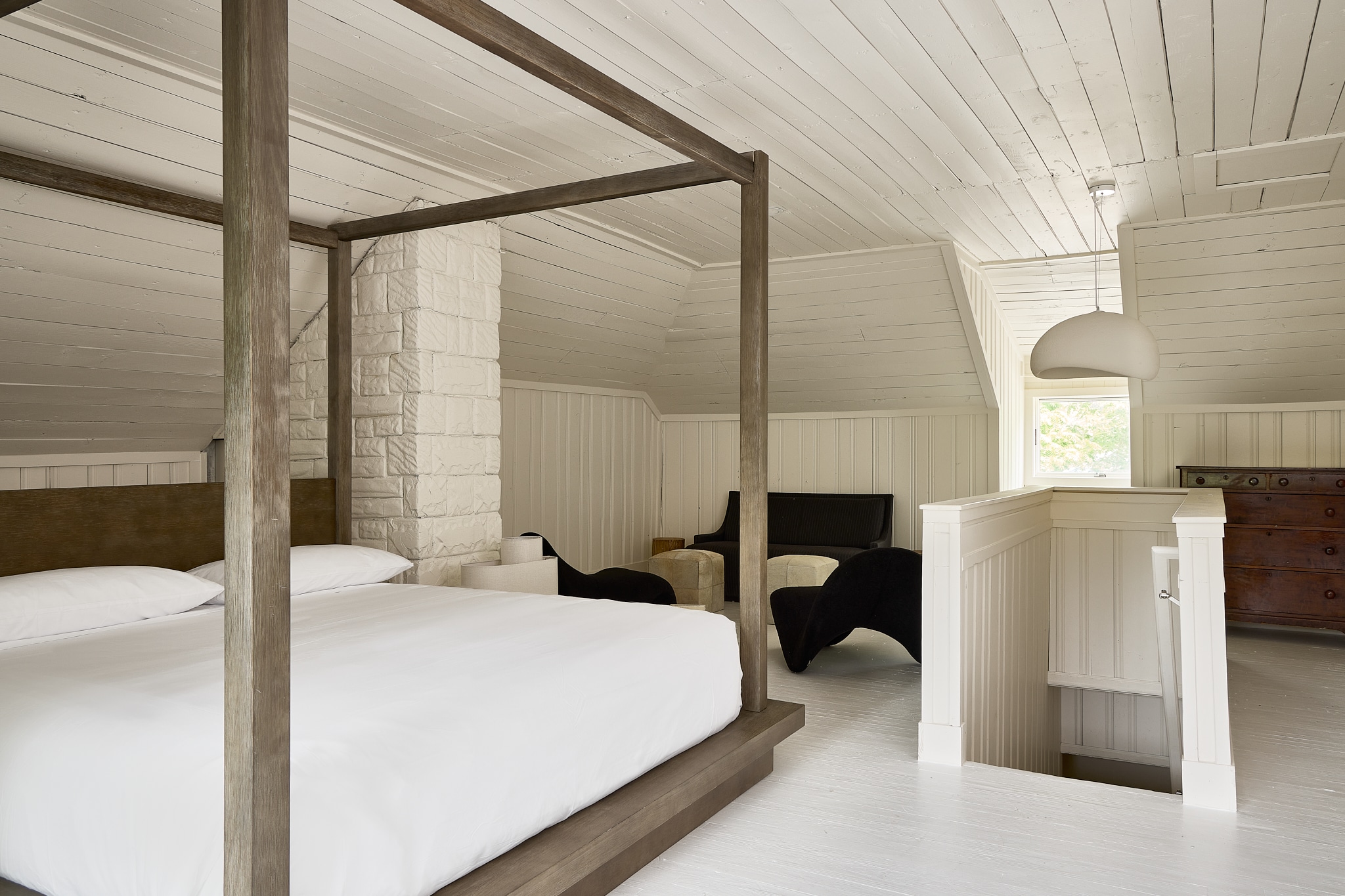 A bright and airy room with a four-poster bed, white bedding, and a stone wall.
