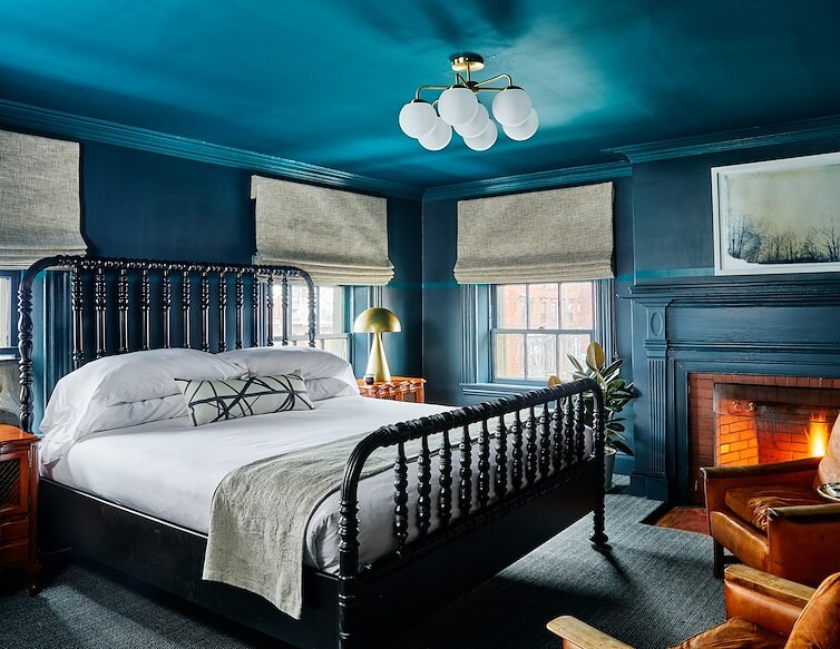 Blind Tiger guest room with deep blue walls, a four-poster bed, leather seating and a fireplace.