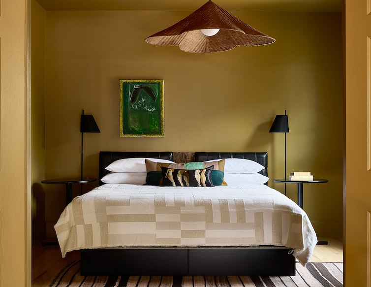 Blind Tiger guest room with warm olive walls, a king bed, contemporary artwork and a woven pendant light.