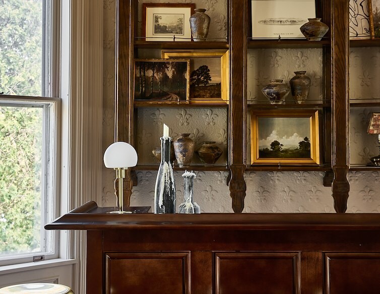 Blind Tiger Burlington bar with dark wood cabinetry, brass stools, vintage artwork and decorative ceramics.