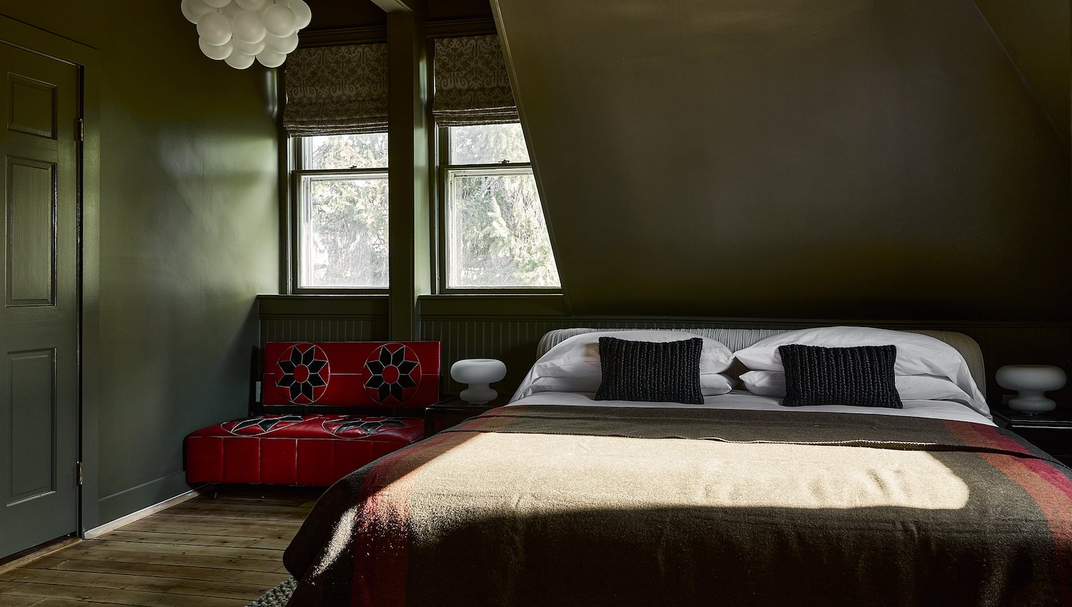 Moody Blind Tiger guest room with dark green walls, a king bed and bold red accent seating.