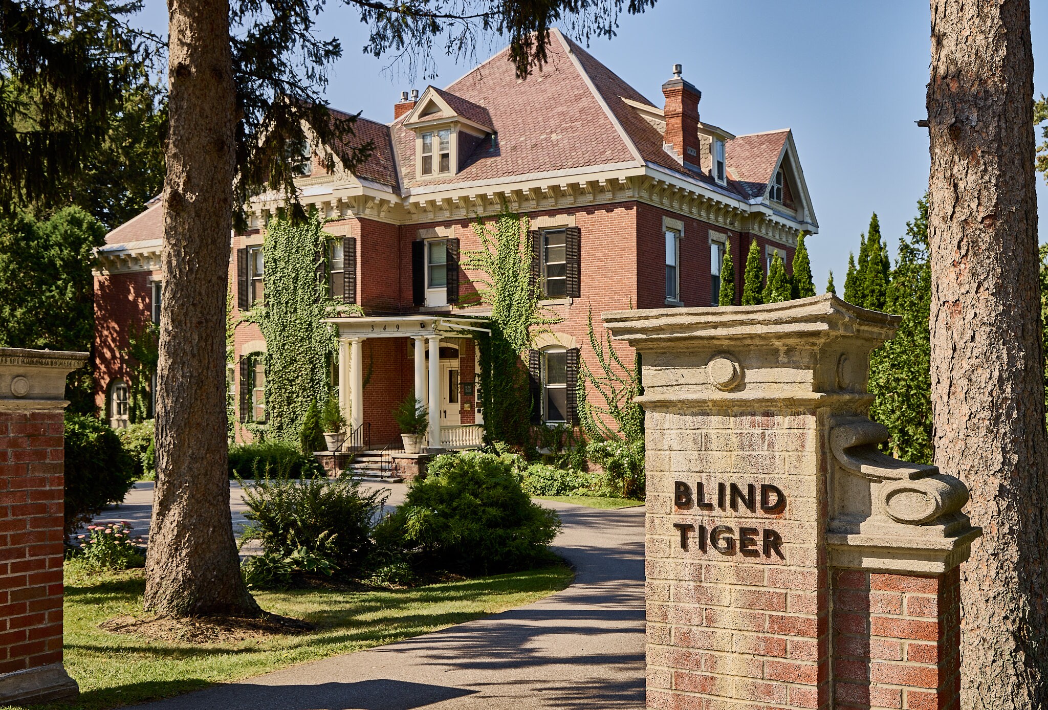 Historic brick exterior of Blind Tiger Burlington in Burlington, VT, surrounded by mature trees and greenery.