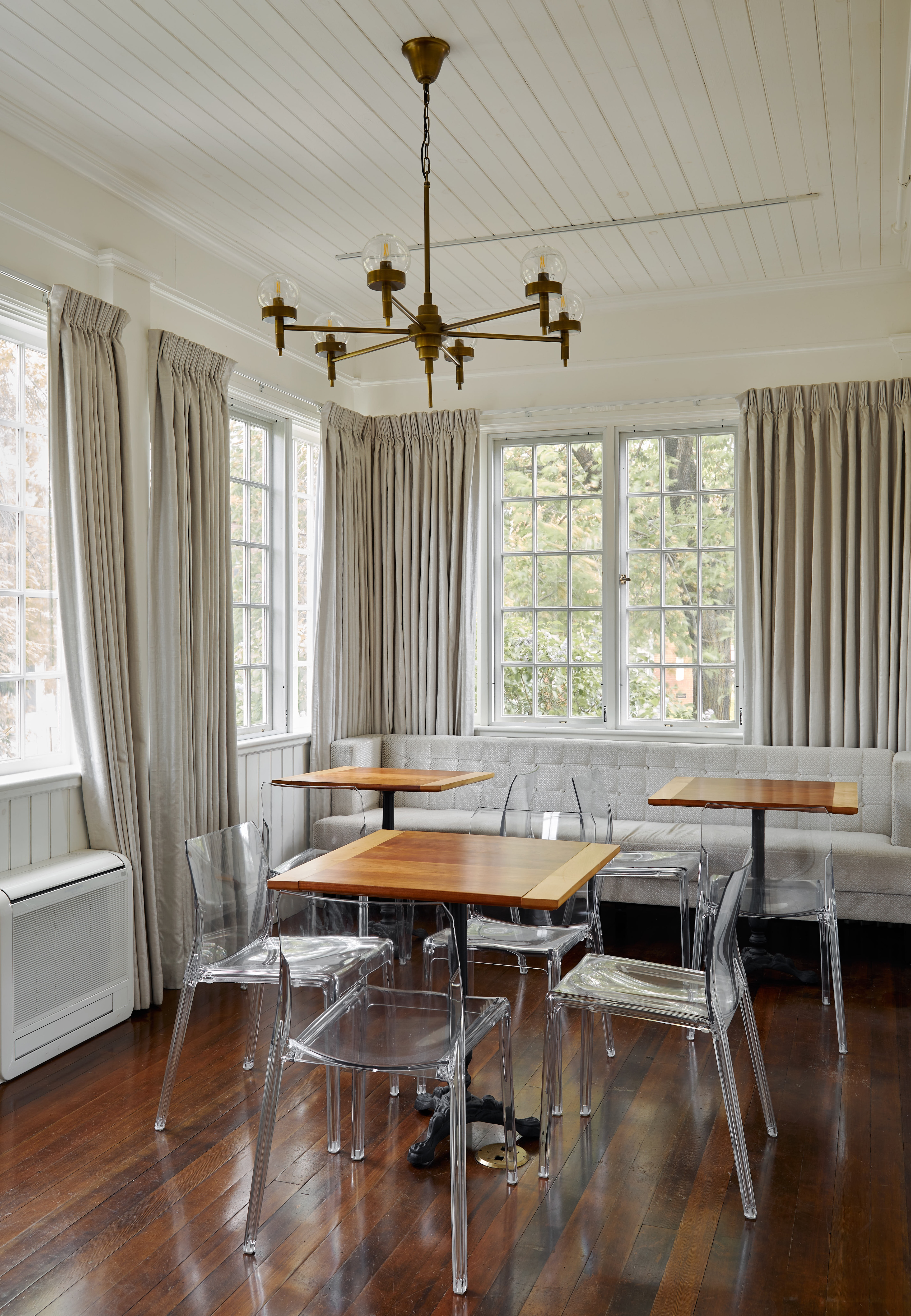 A bright and airy dining area with wooden tables, clear chairs, and white booth seating.