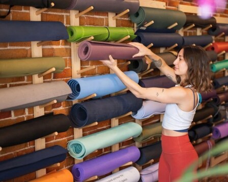  woman placing rolled yoga mat on wall of equipment 