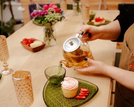  person pouring a pot of tea into green glass with decor on table 