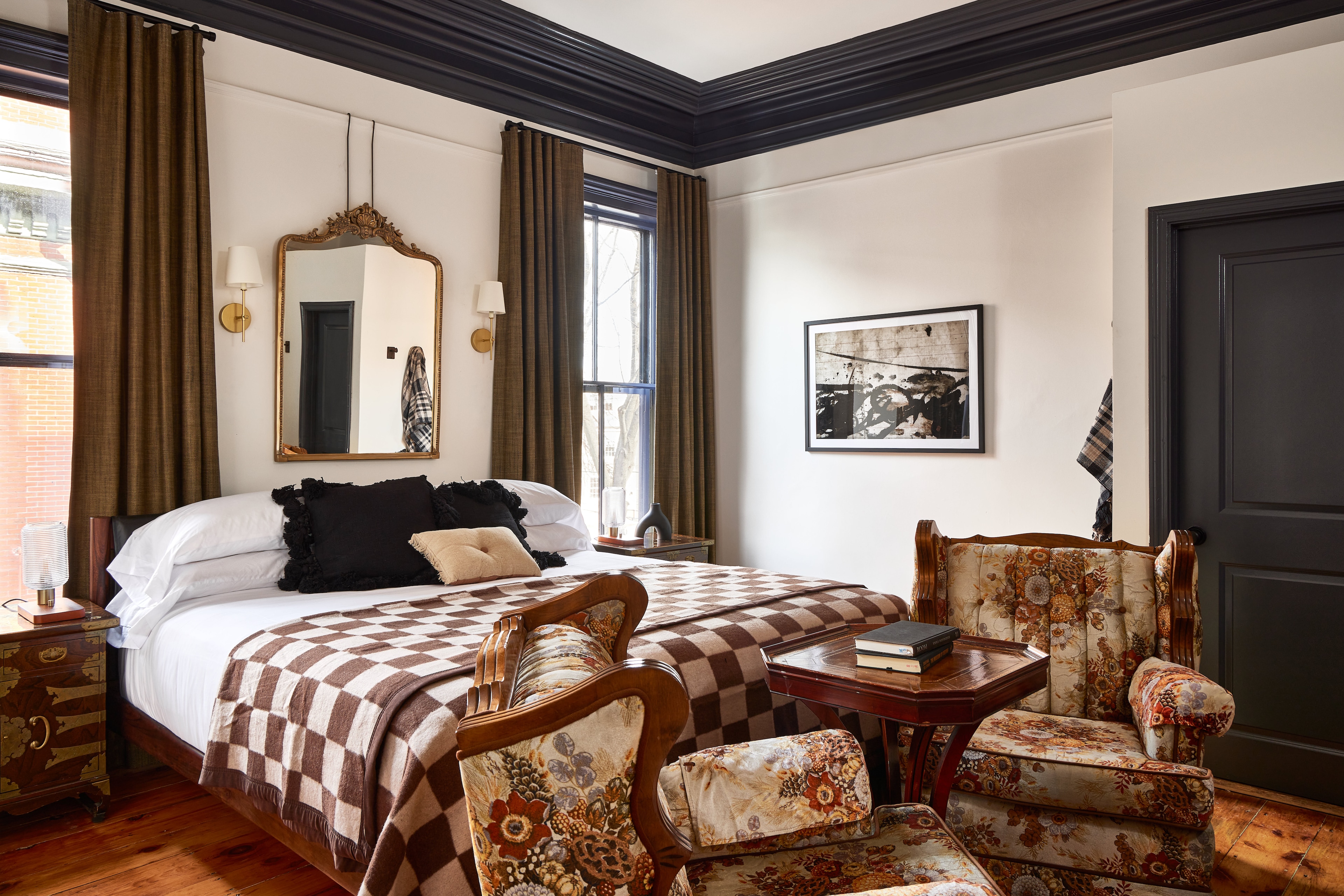 A wide view of a hotel room with a bed, two chairs, a table, a mirror, and a window.