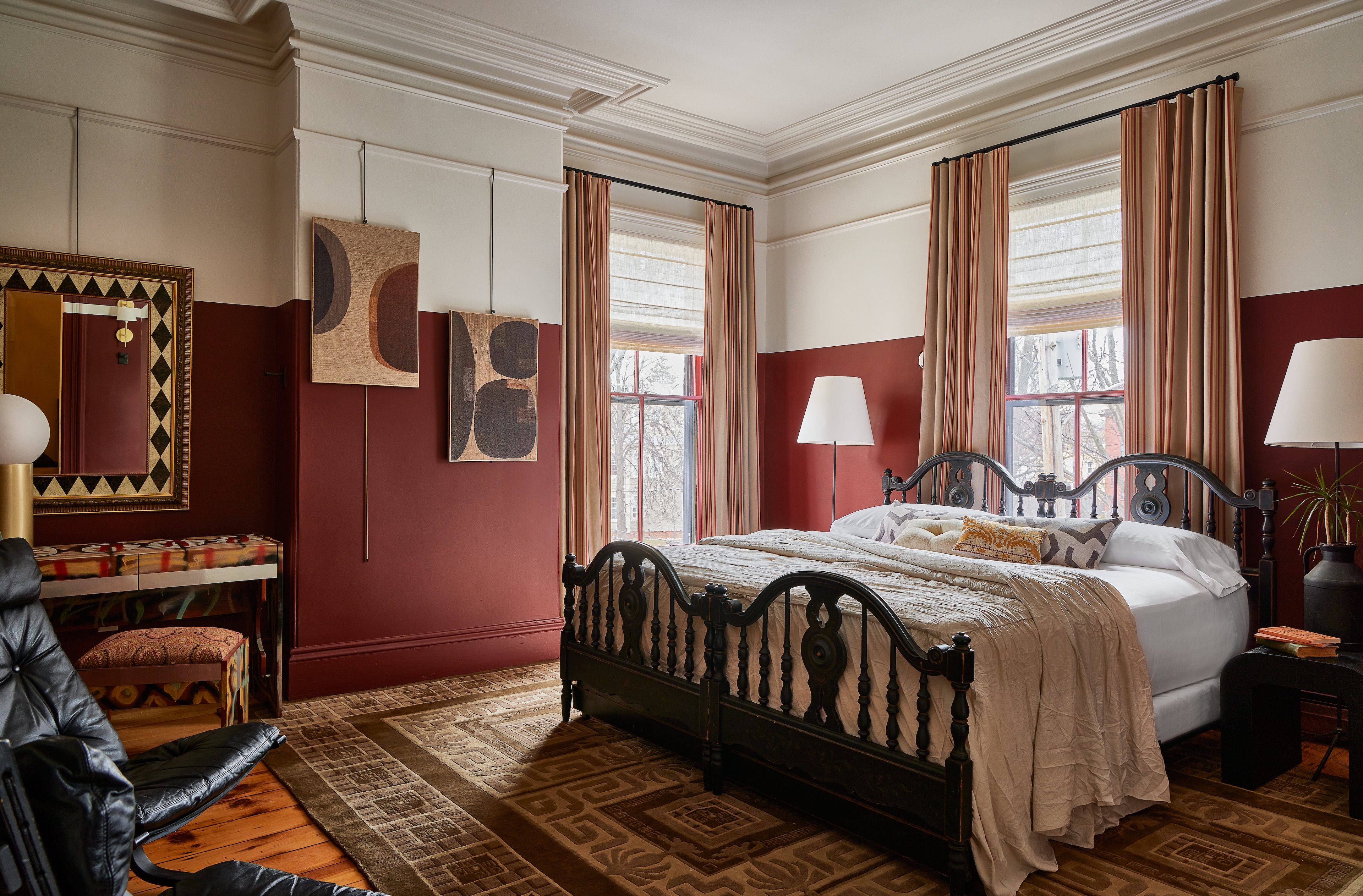 A wide view of a bedroom with a bed, two windows, a desk, and a mirror.