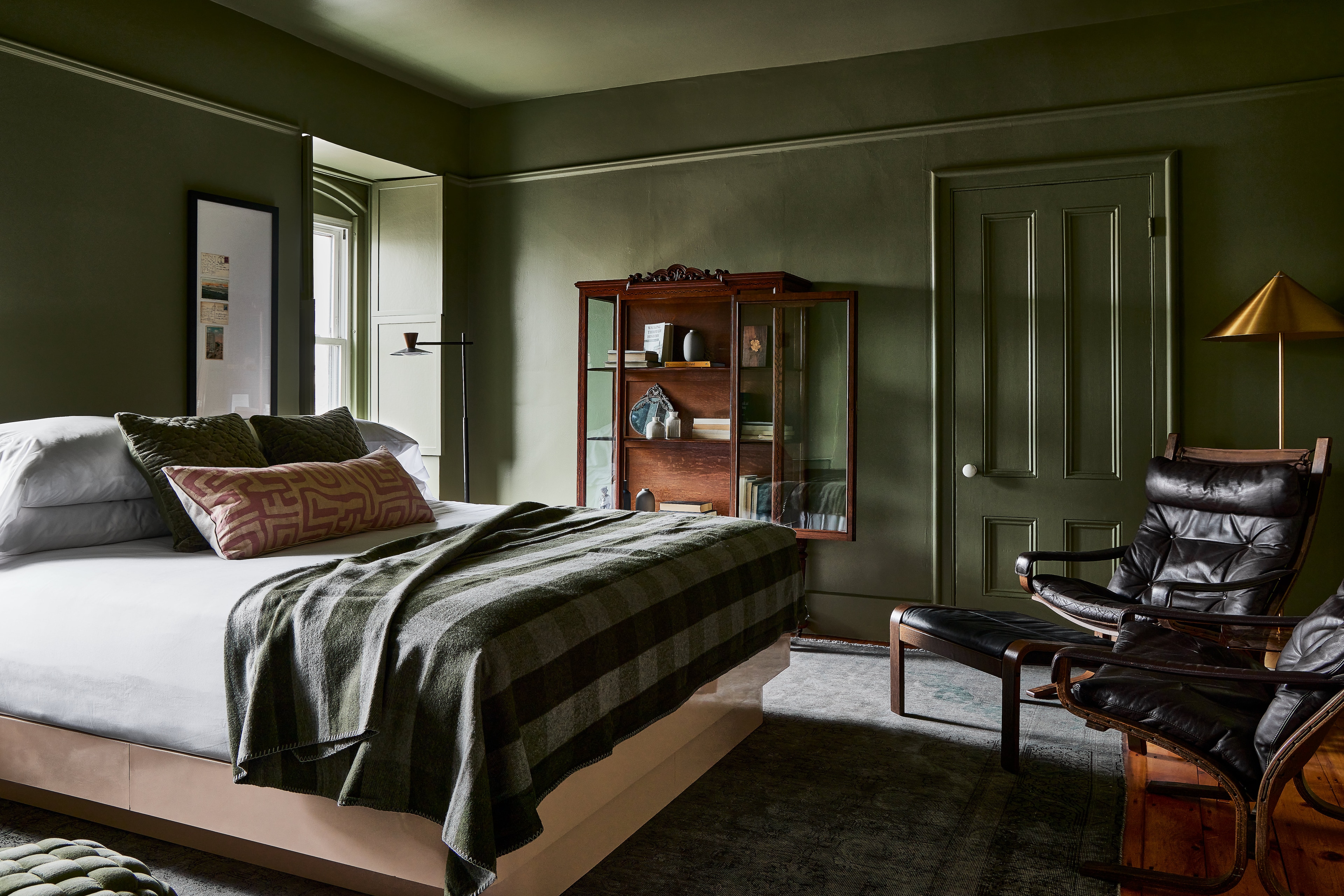 A wide-angle view of a bedroom with a bed, chair, door, window, and bookshelf.