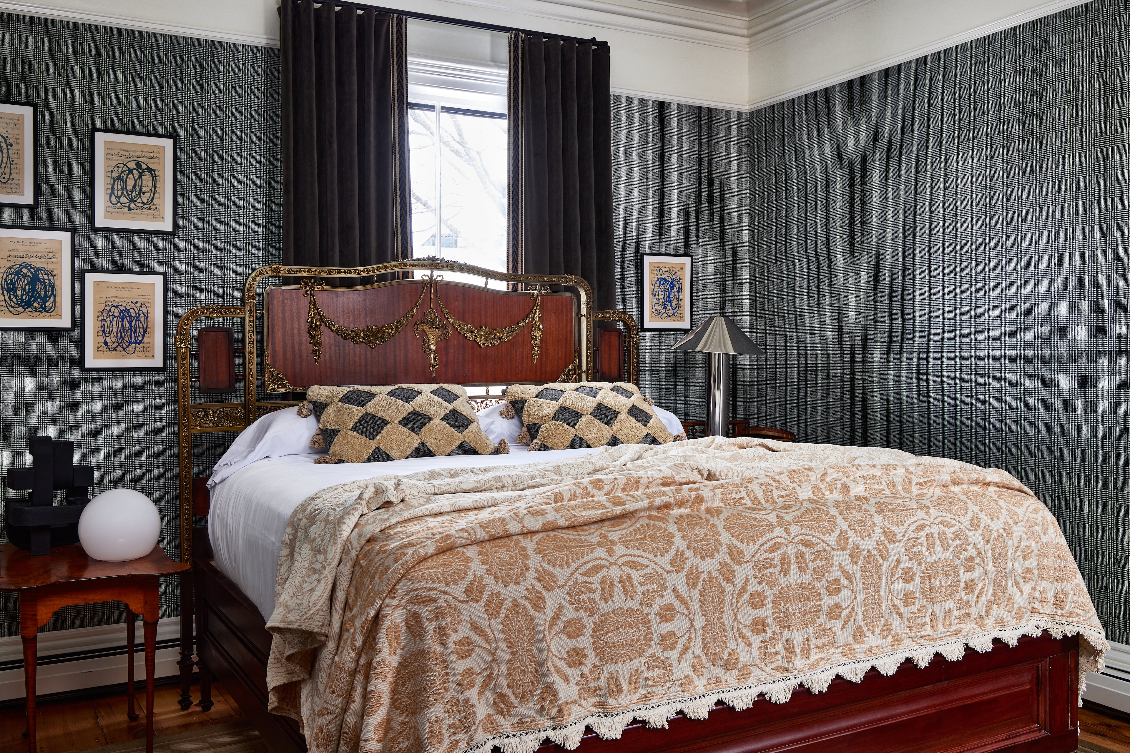 A bed with a large ornate headboard, pillows, and a blanket in a room with wallpaper and a window.