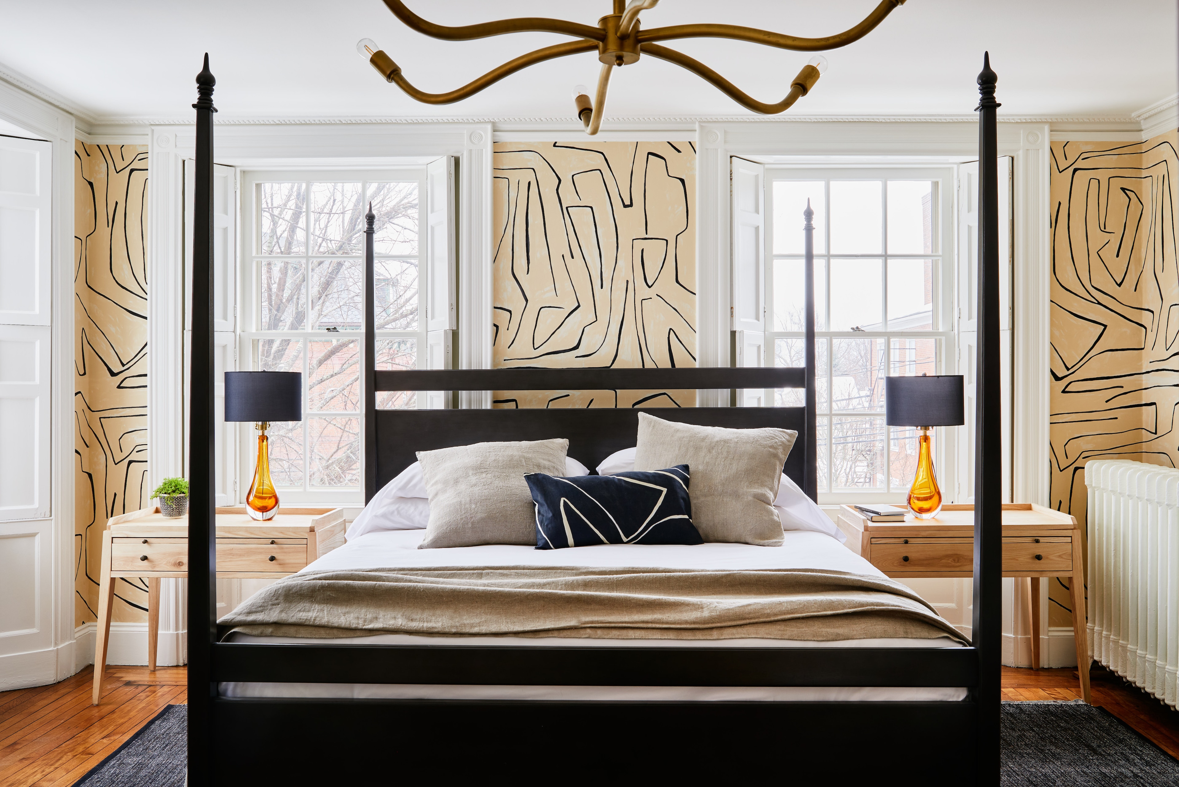A four-poster bed with a white comforter and several pillows is centered in a room with a window and nightstands.